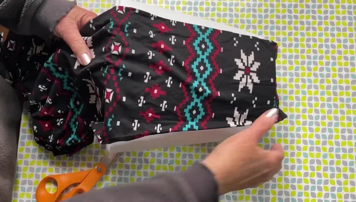 Slide the fabric over the trash can, ensuring a snug fit.