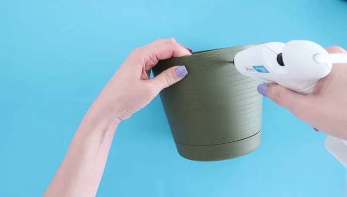 Create hanging planters by burning holes in Dollar Tree planters, adding jute cords, and decorating.